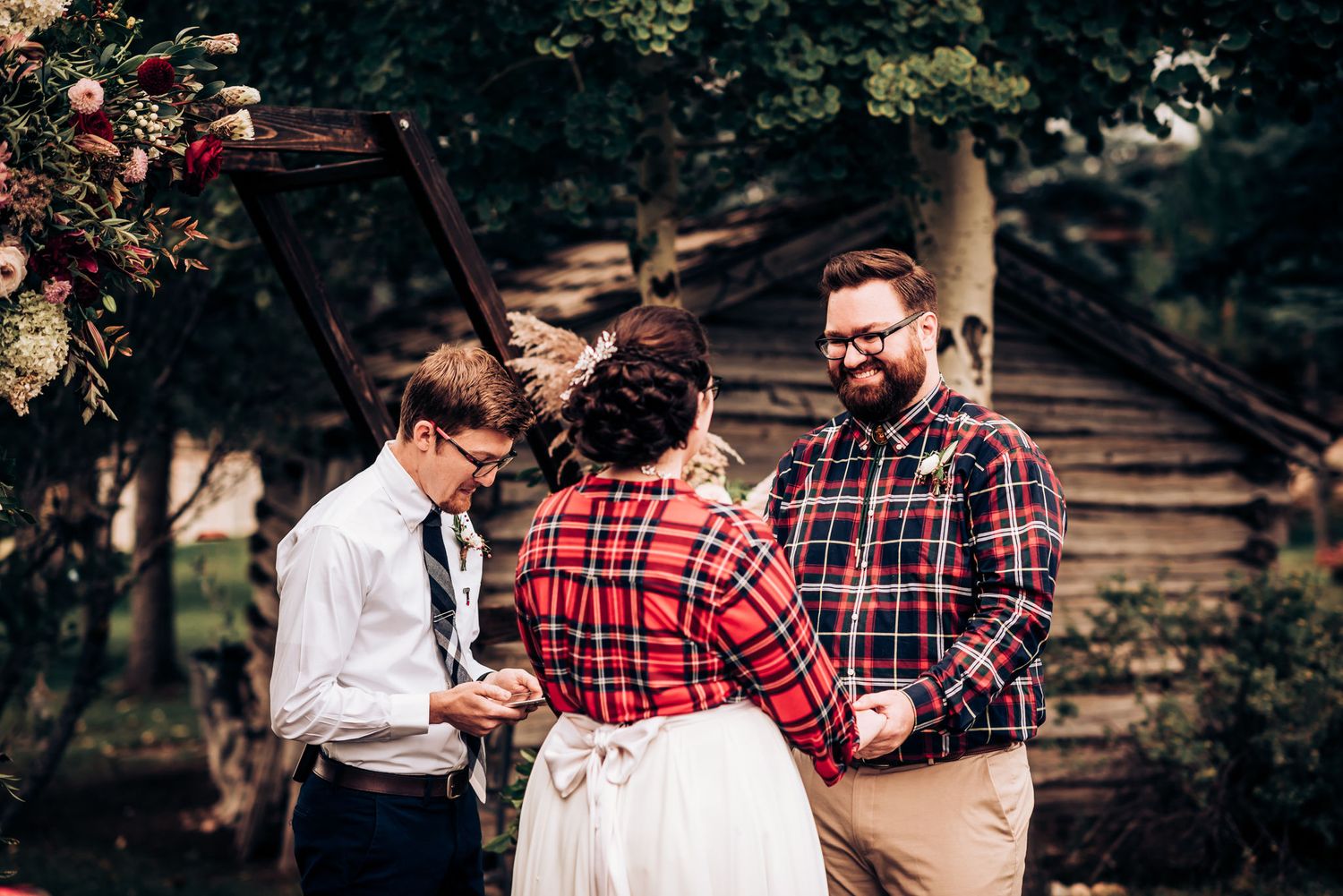 Wedding ceremony participants gather near a decorated wooden cabin for an intimate outdoor celebration.