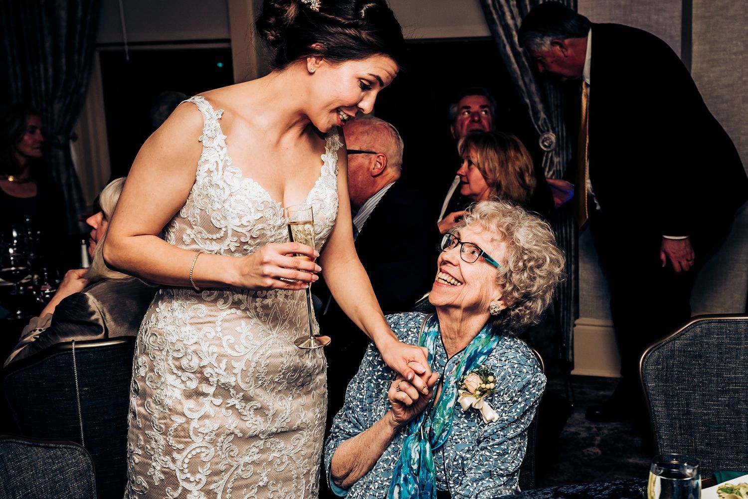 A touching candid moment between a bride in lace and an elderly guest during a wedding reception.