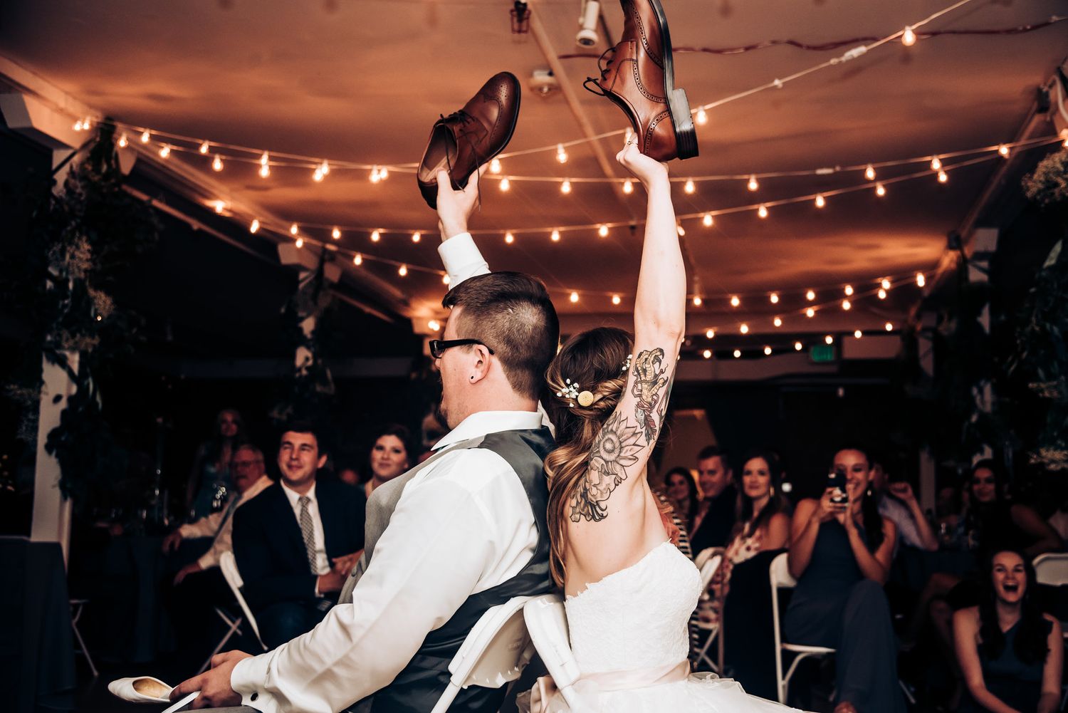 Newlyweds perform an energetic dance move under string lights at their reception.