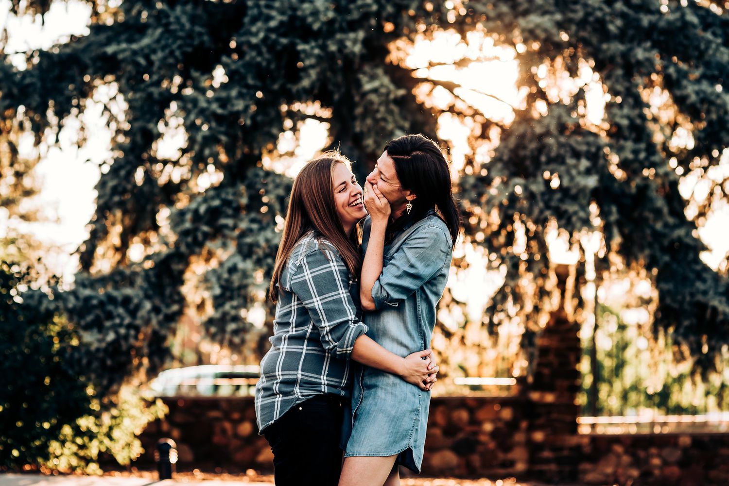 A tender moment captured between two people against a backdrop of sunlit pine trees.
