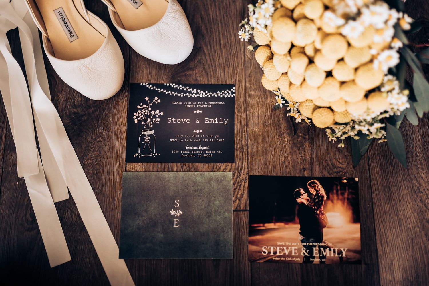 Wedding invitation suite with shoes and floral details on wooden surface.