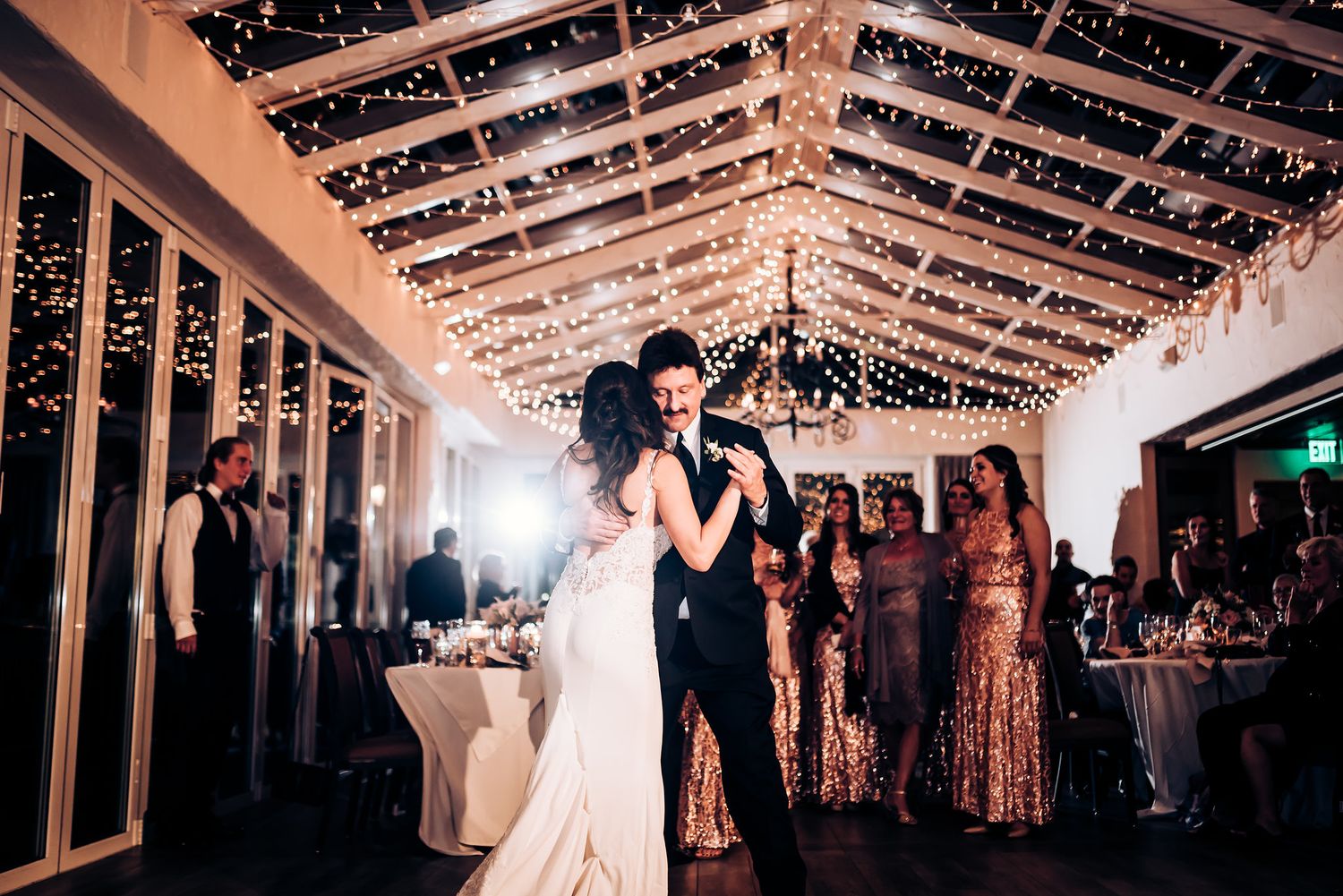 Wedding couple dances in white venue decorated with romantic string lights overhead.