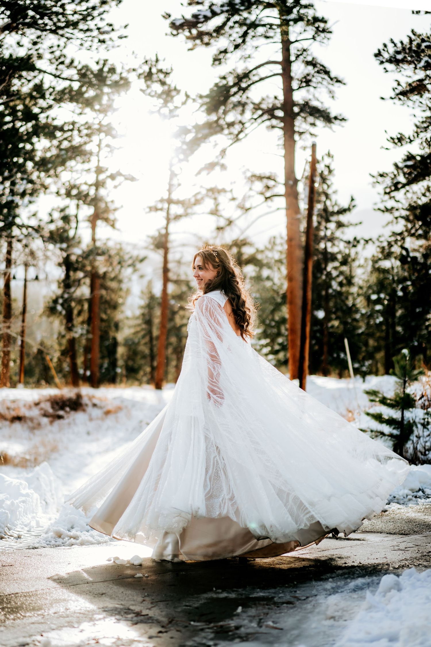 Bride in flowing white gown twirling in snowy winter forest setting.