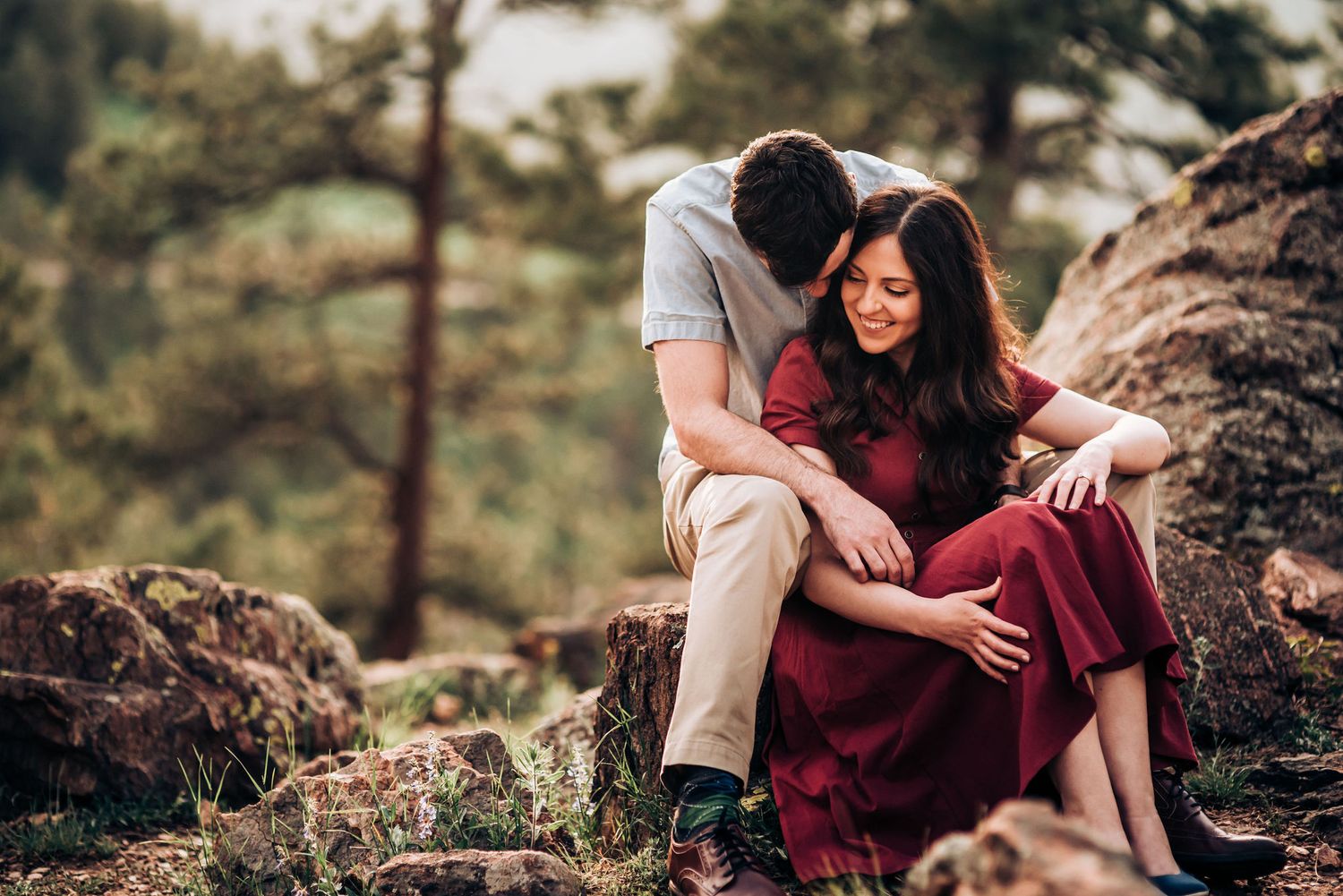 A romantic couple shares a tender moment while sitting on rocky mountain terrain.