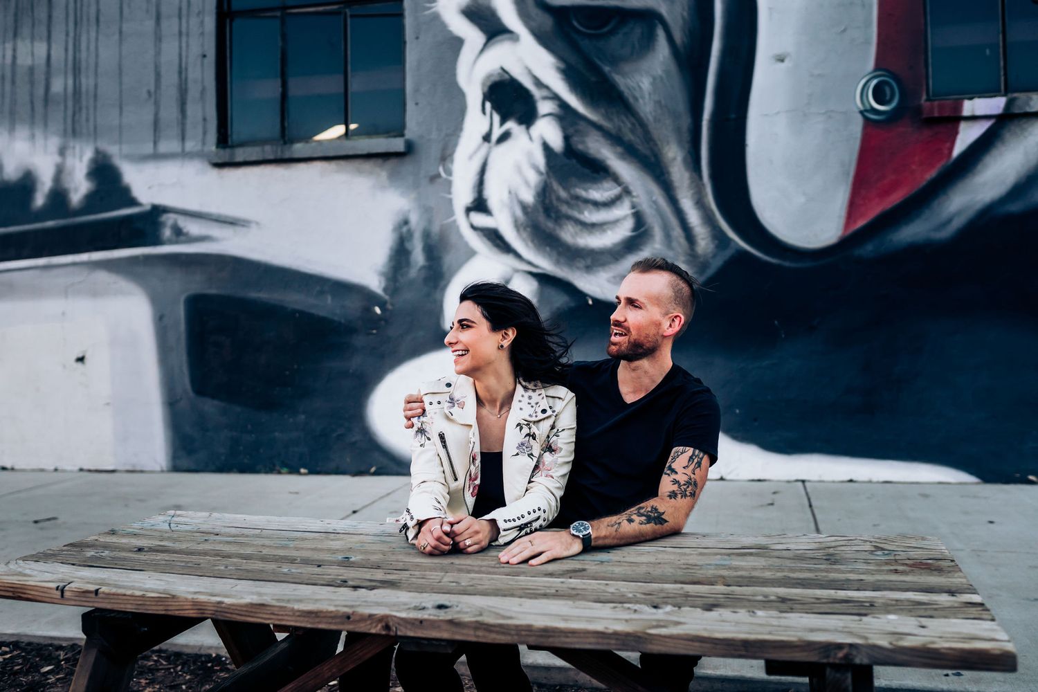 Couple sits on wooden bench in front of large monochrome street art mural.