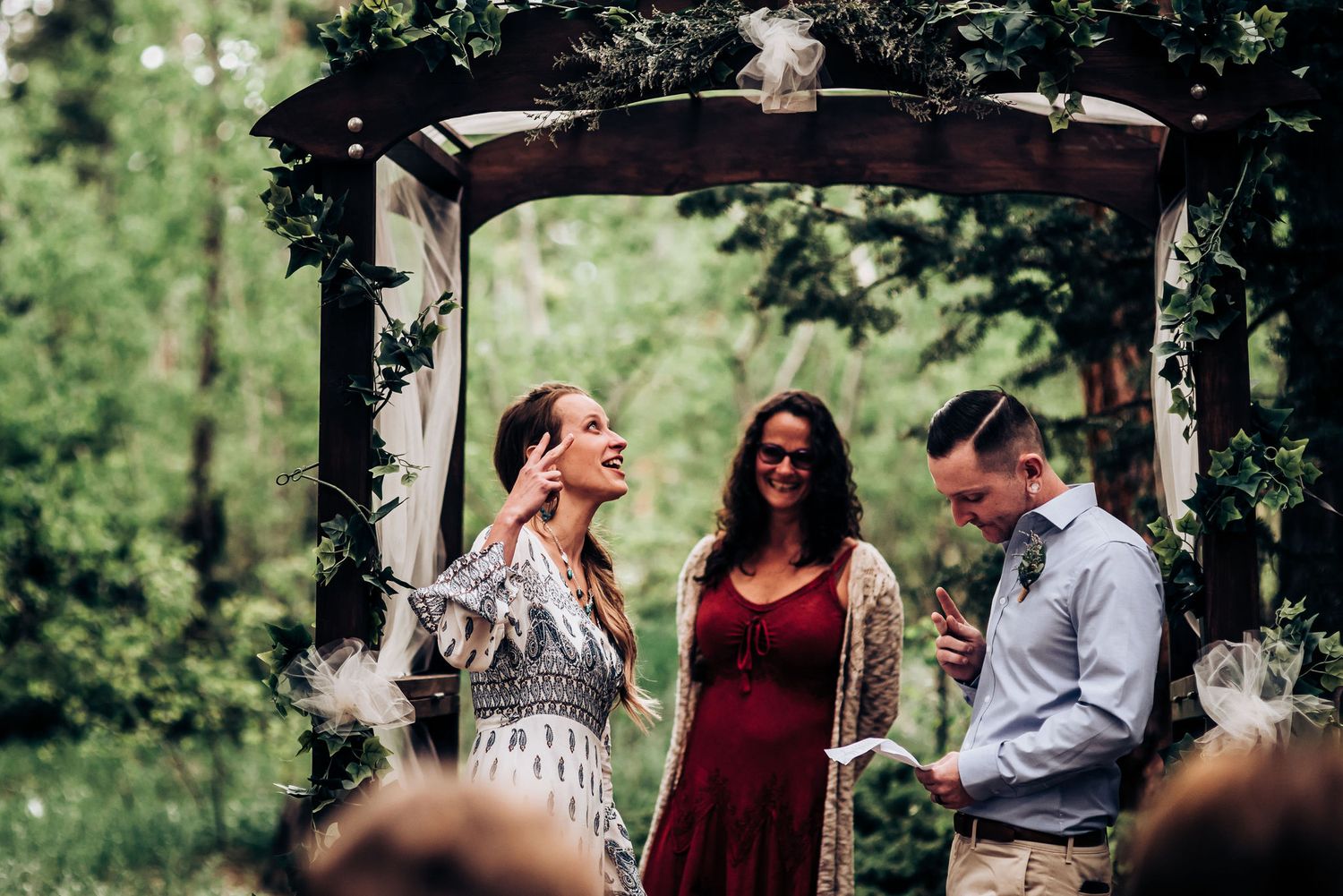 A touching moment during a forest wedding ceremony under a decorated wooden arch.