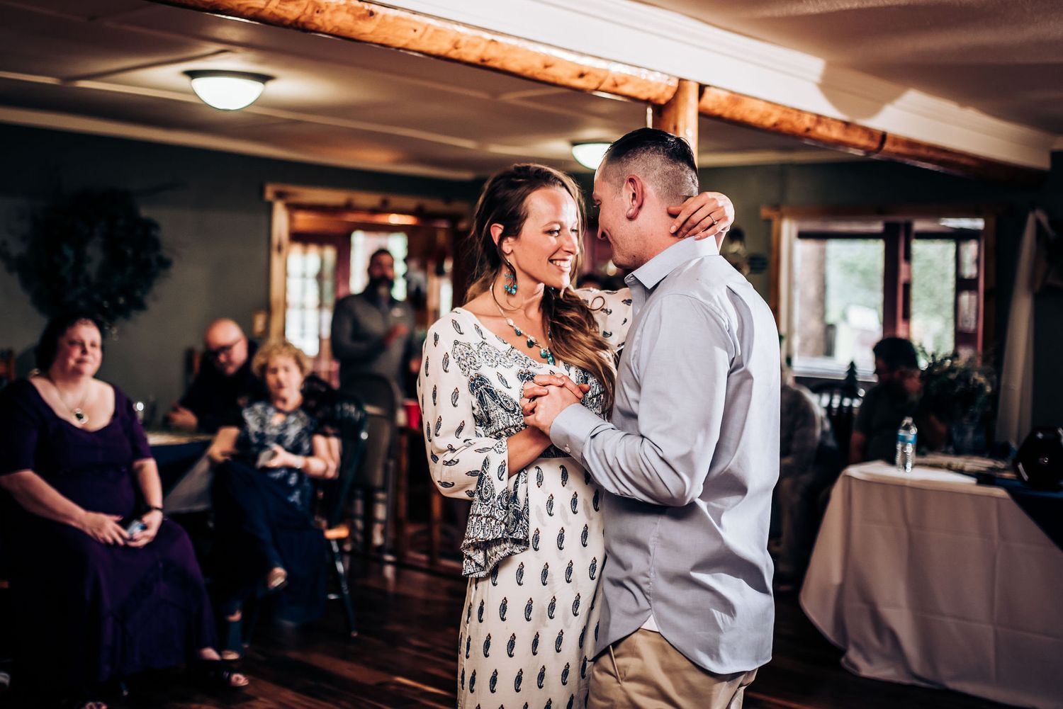 A couple embraces during their first dance at a wedding reception venue with wooden beams.