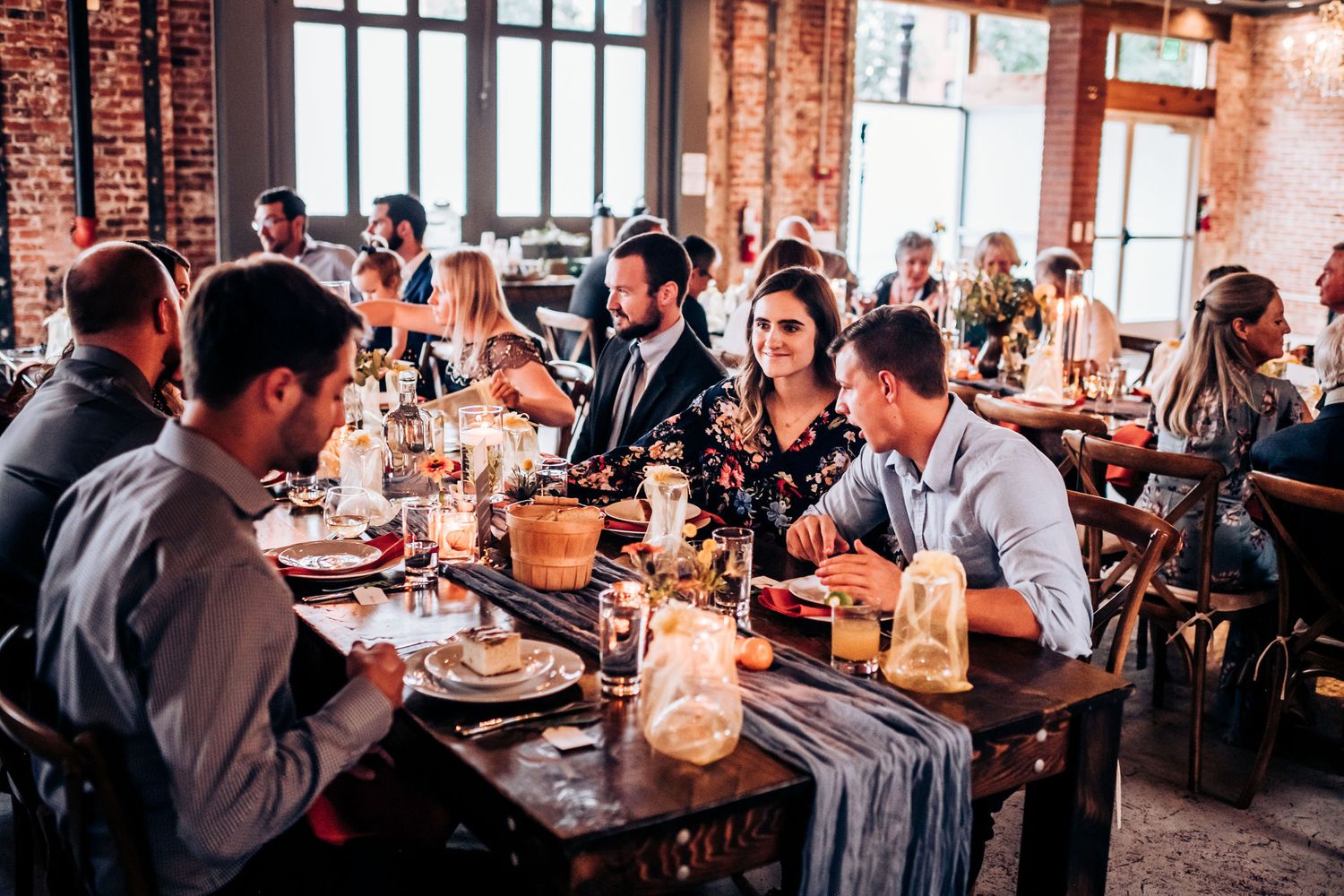 Friends gathered around a rustic table enjoying dinner in a trendy brick-walled restaurant.