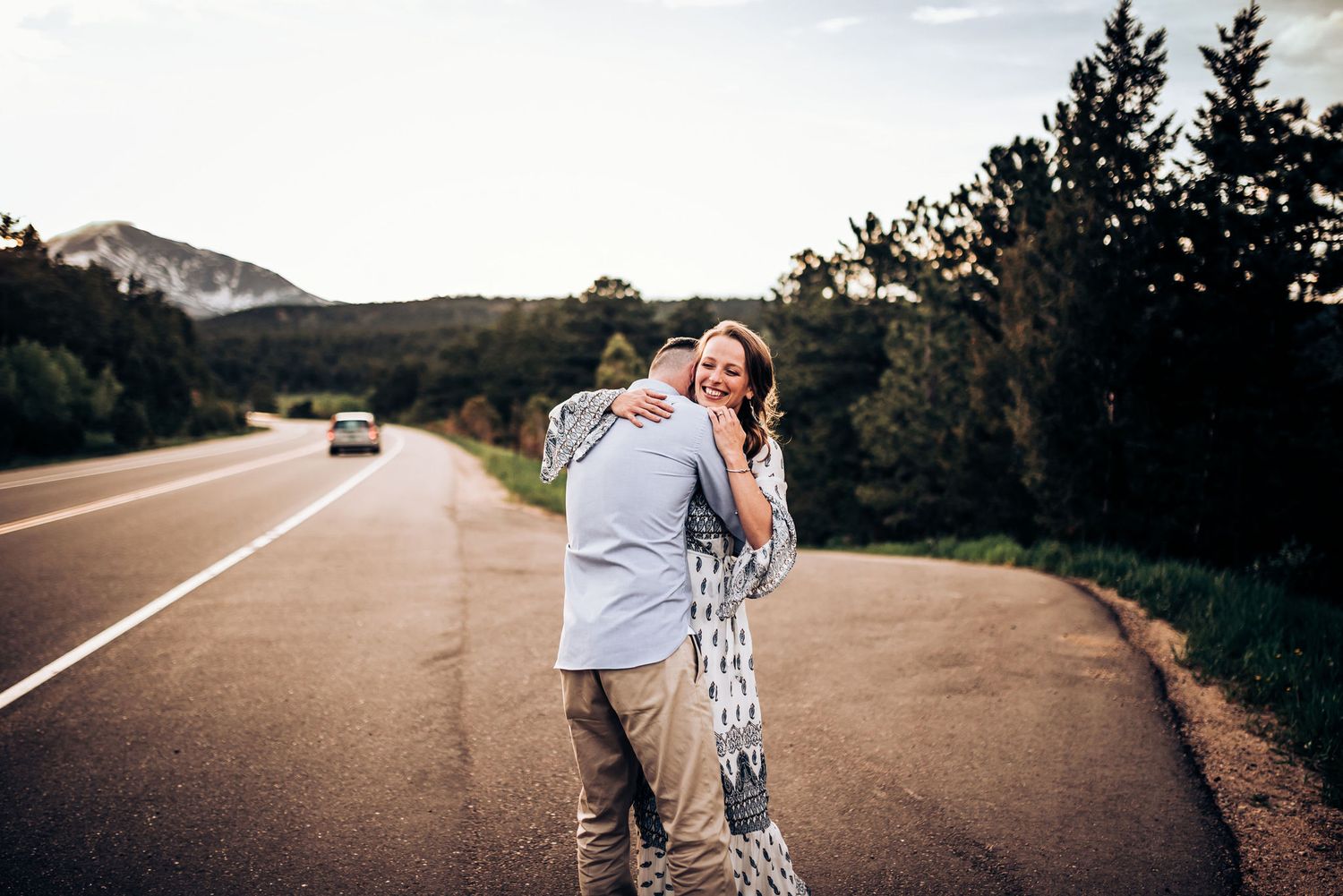 Couple sharing tender moment on scenic mountain road with mountains in background.