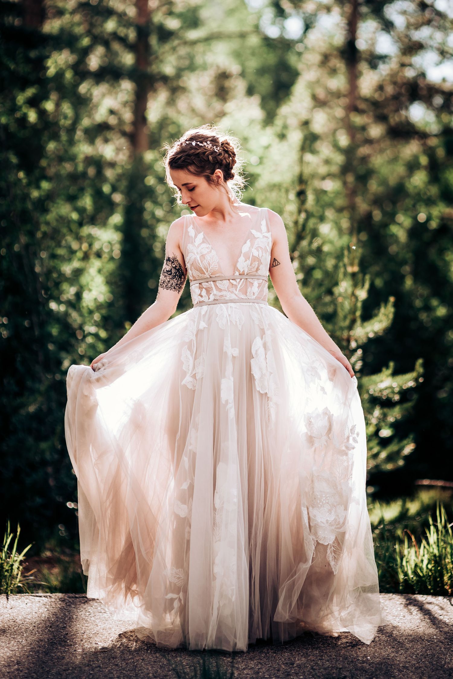 A bride in a flowing blush wedding gown twirls in the dappled forest light.