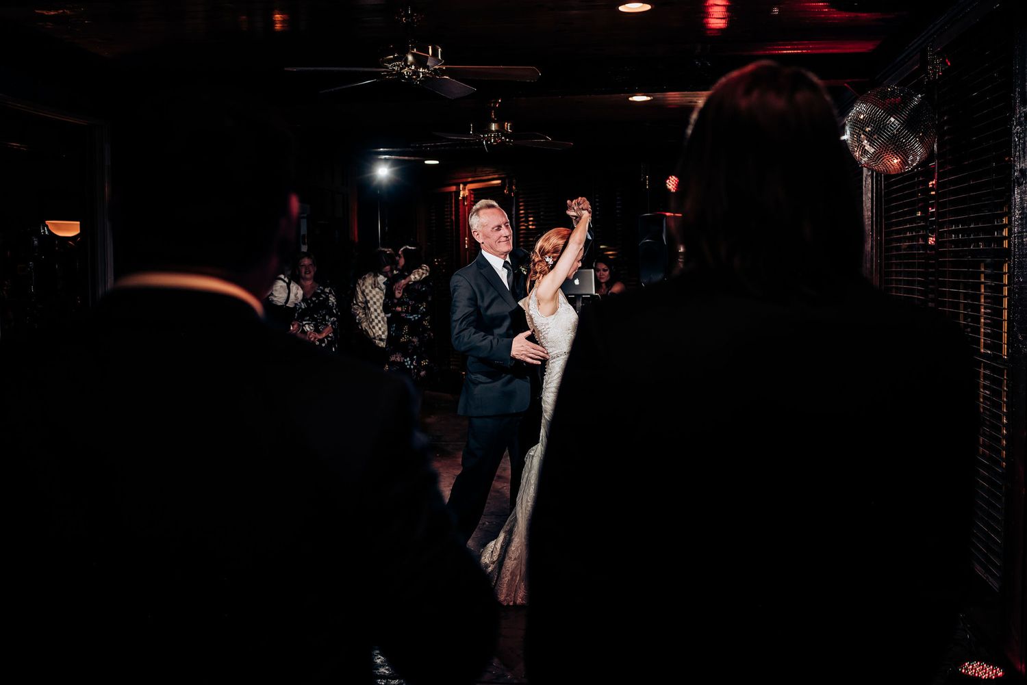 A couple dances in silhouette against dark dramatic lighting at their wedding reception.
