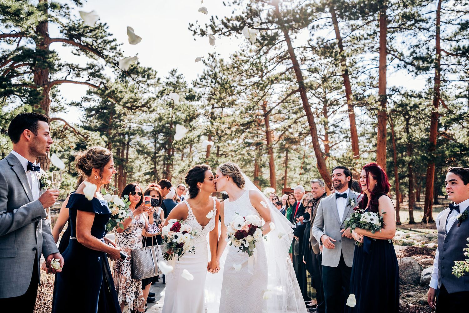Guests celebrate during an outdoor mountain wedding ceremony surrounded by tall pine trees.