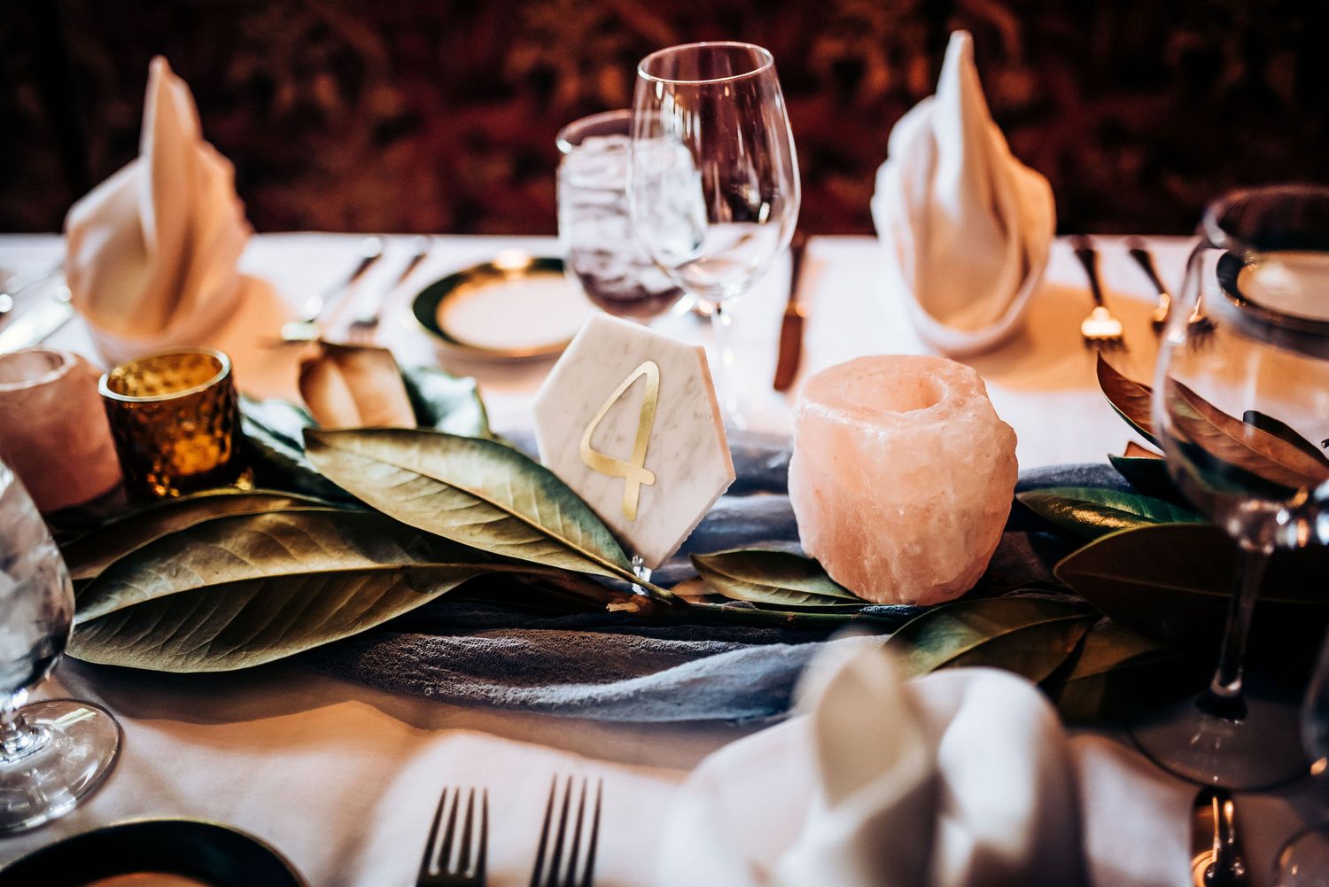 Wedding table decor with folded napkins, wine glasses and magnolia leaves.