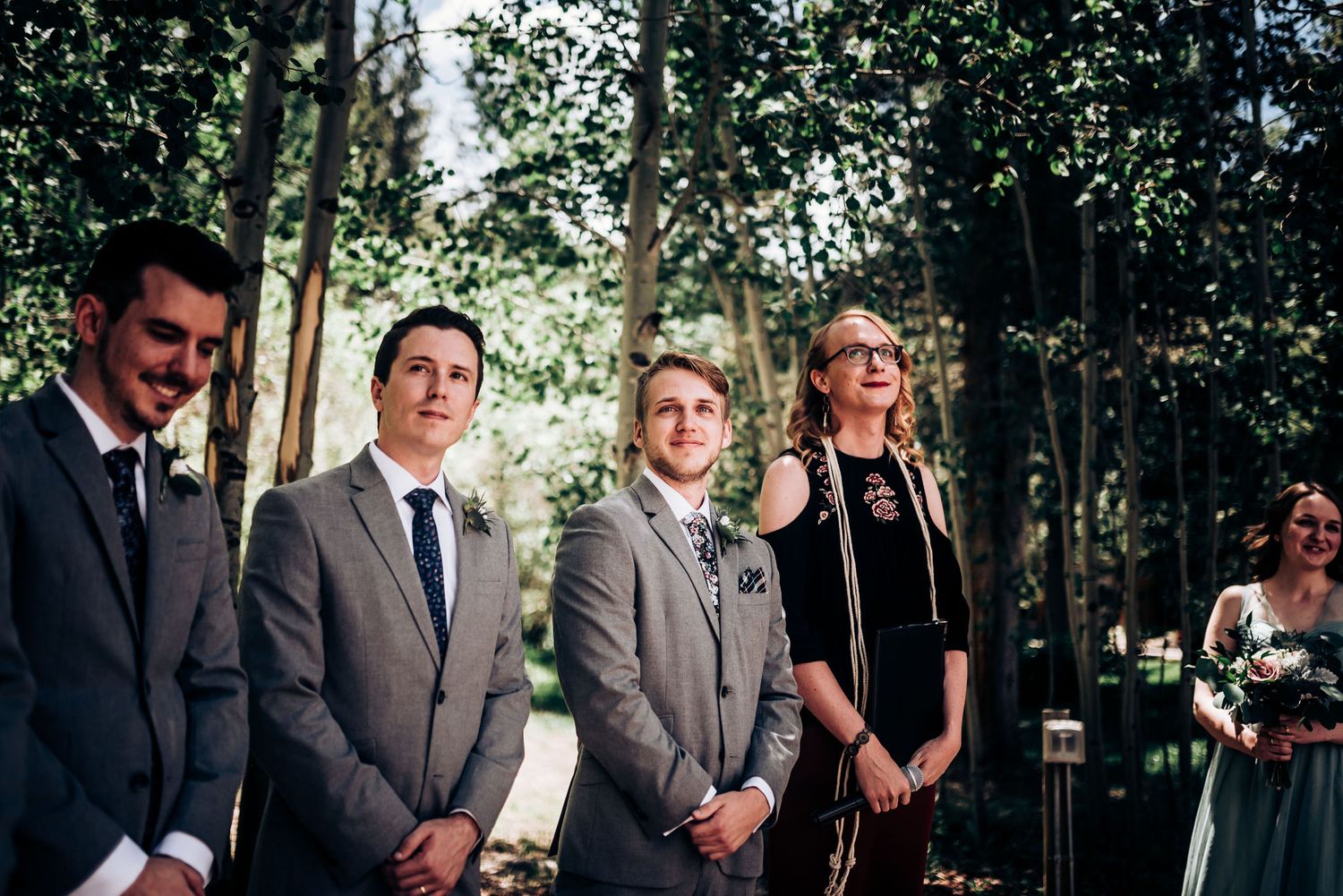 Wedding party members standing in forest setting wearing formal attire.