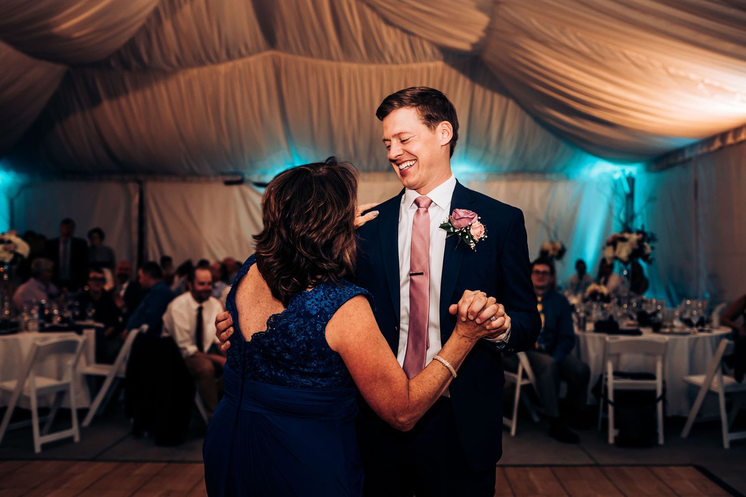 A formal dance at a wedding reception with guests seated at tables in the background.