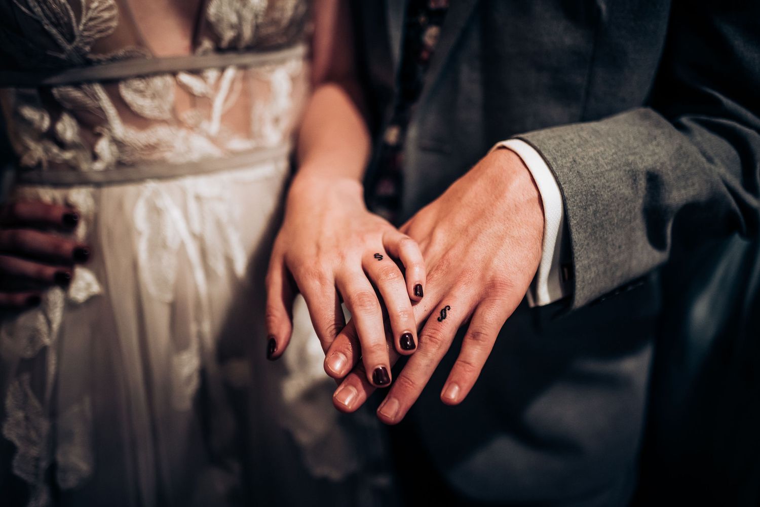 Close-up of newlyweds' hands showing off wedding rings against formal attire.