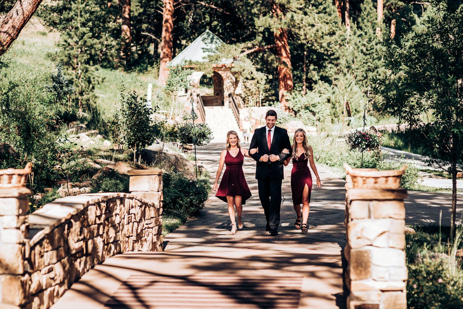 Wedding attendants walk down a stone pathway surrounded by pine trees and garden landscaping.