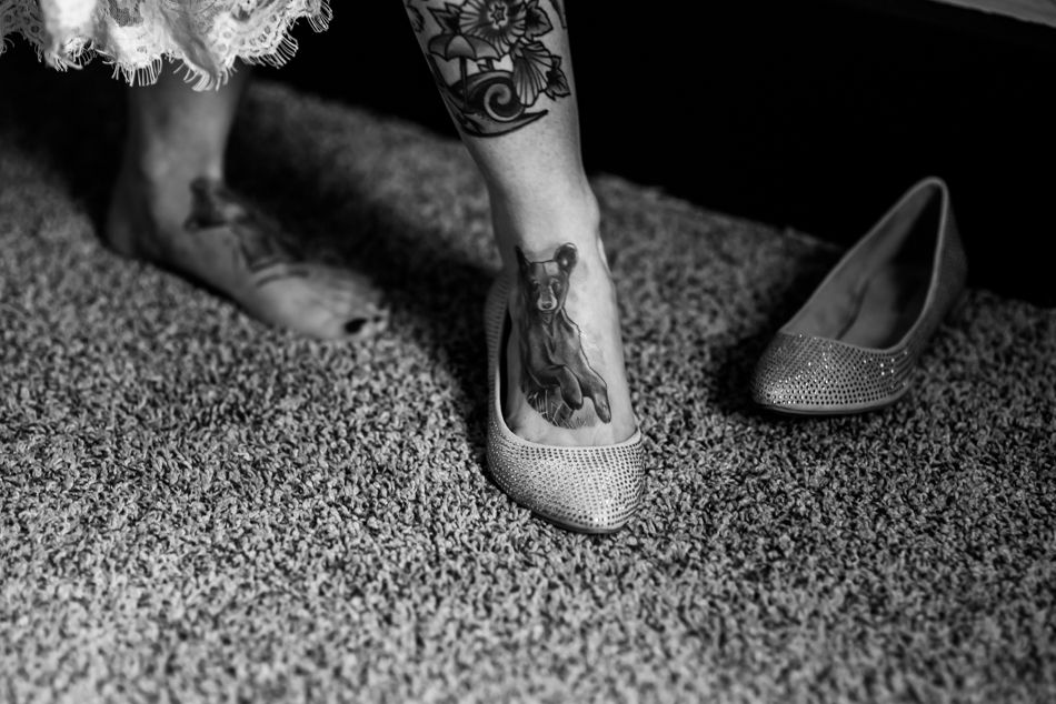 Close-up of tattooed feet slipping into elegant bridal flats on carpet.