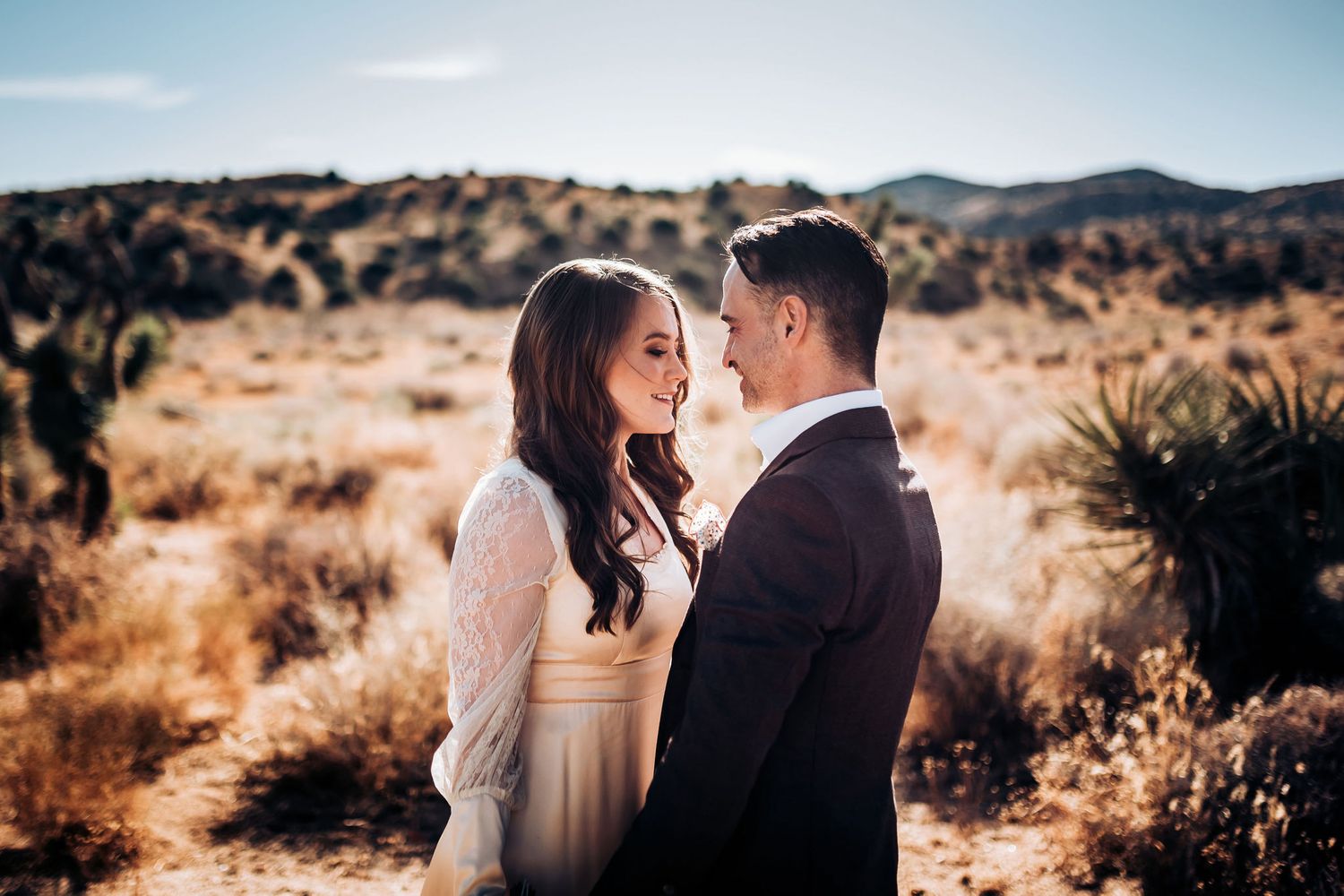 Intimate moment between couple in wedding attire against desert landscape.