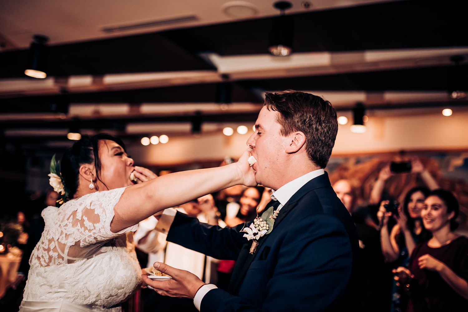 Playful cake-feeding moment between couple during wedding reception celebration.