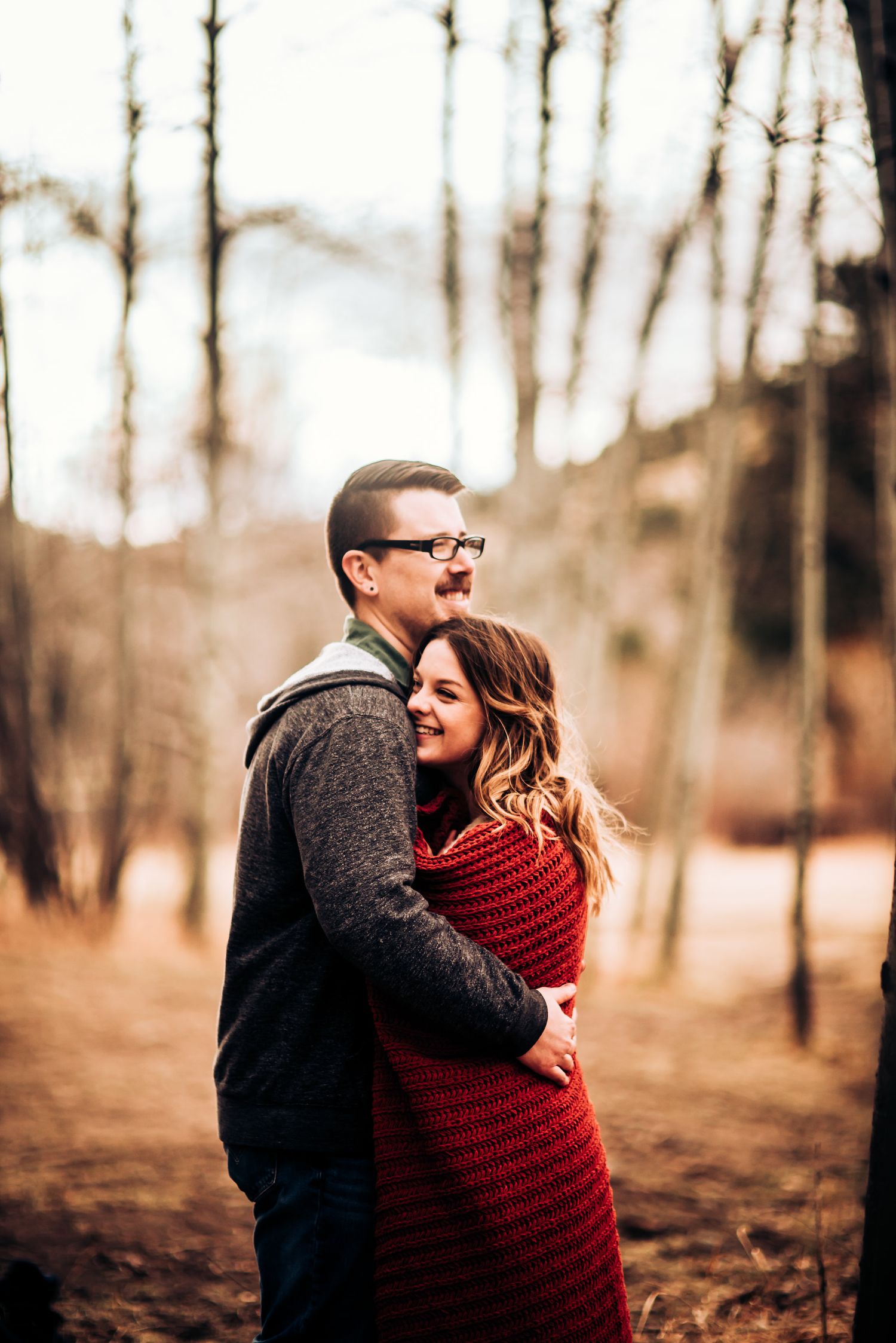 An intimate embrace between a couple in a wooded autumn setting.
