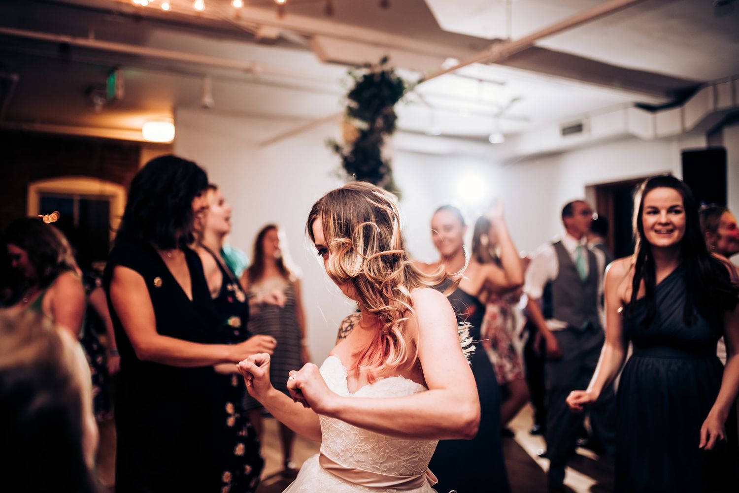 Dancing celebration under warm string lights at indoor wedding reception.