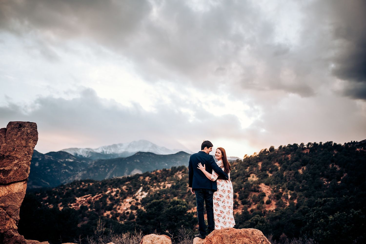 A couple shares an intimate moment on mountain rocks during sunset.