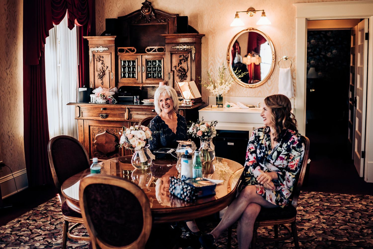Two people enjoy tea and conversation in an elegantly furnished vintage room with ornate furniture.