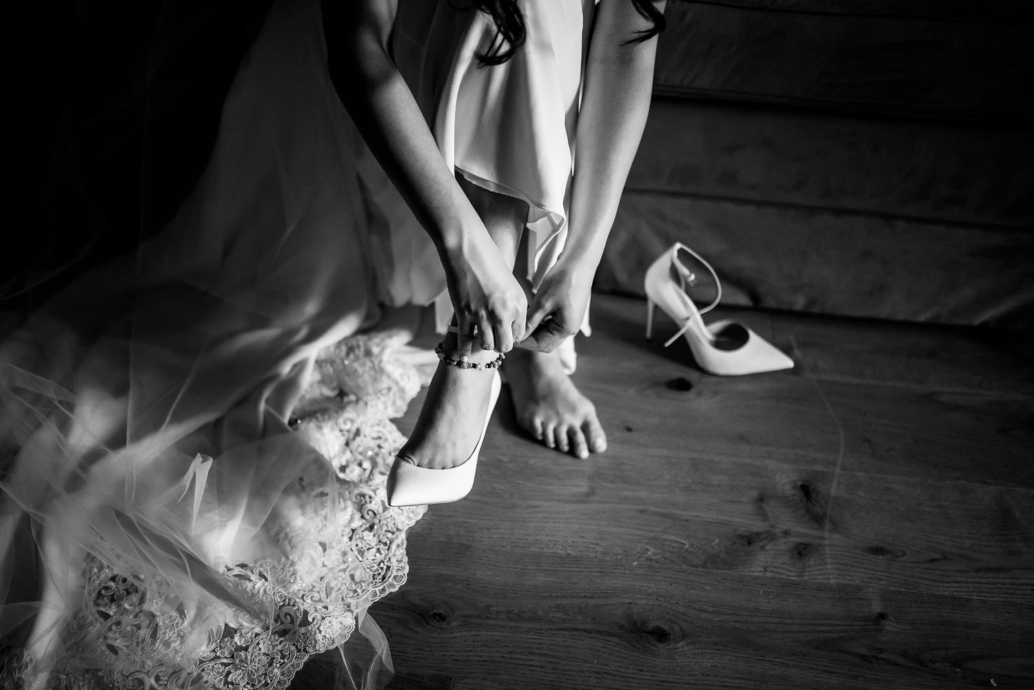 Black and white photo of wedding shoes being fastened with lace dress details.