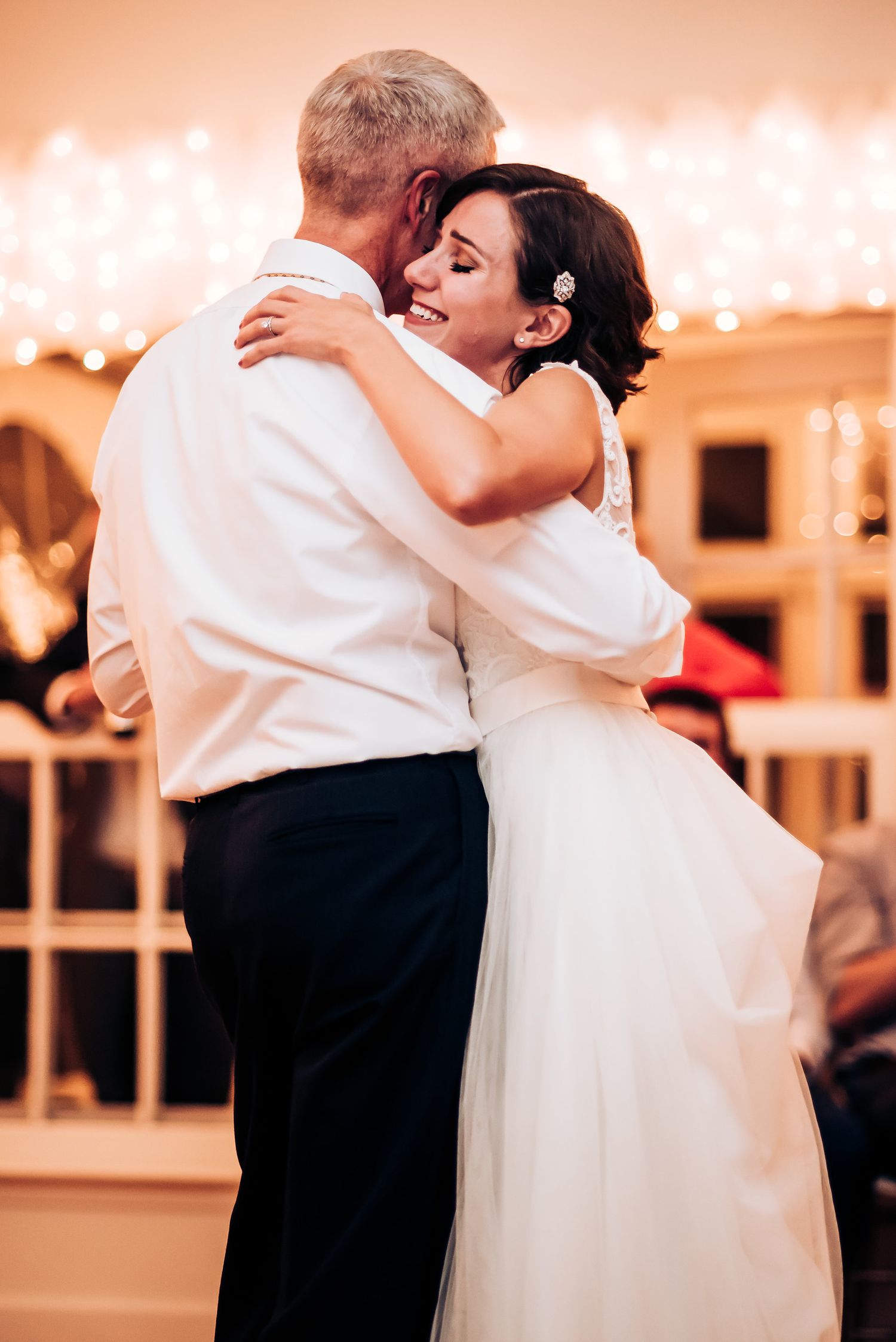 A tender moment captured during a wedding dance with warm lighting and string lights overhead.
