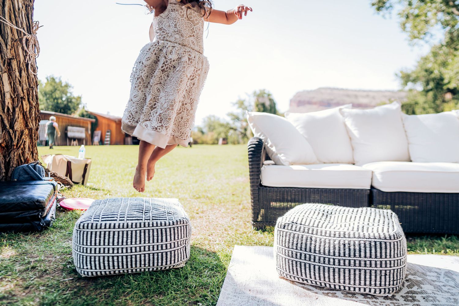 Decorative striped poufs and outdoor lounge furniture arranged on grass near trees.