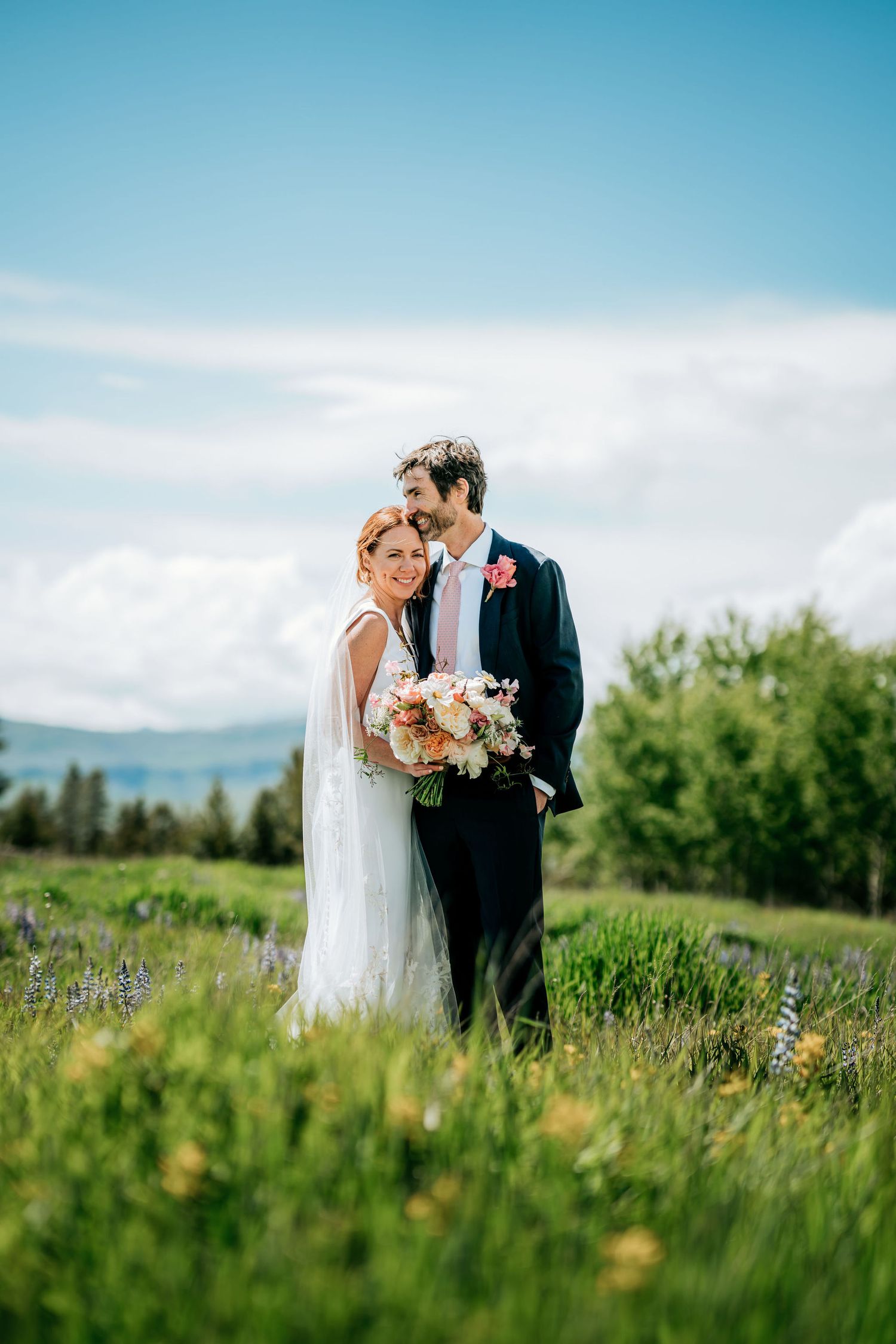 Intimate wedding portrait in a mountain meadow with wildflowers and distant peaks.