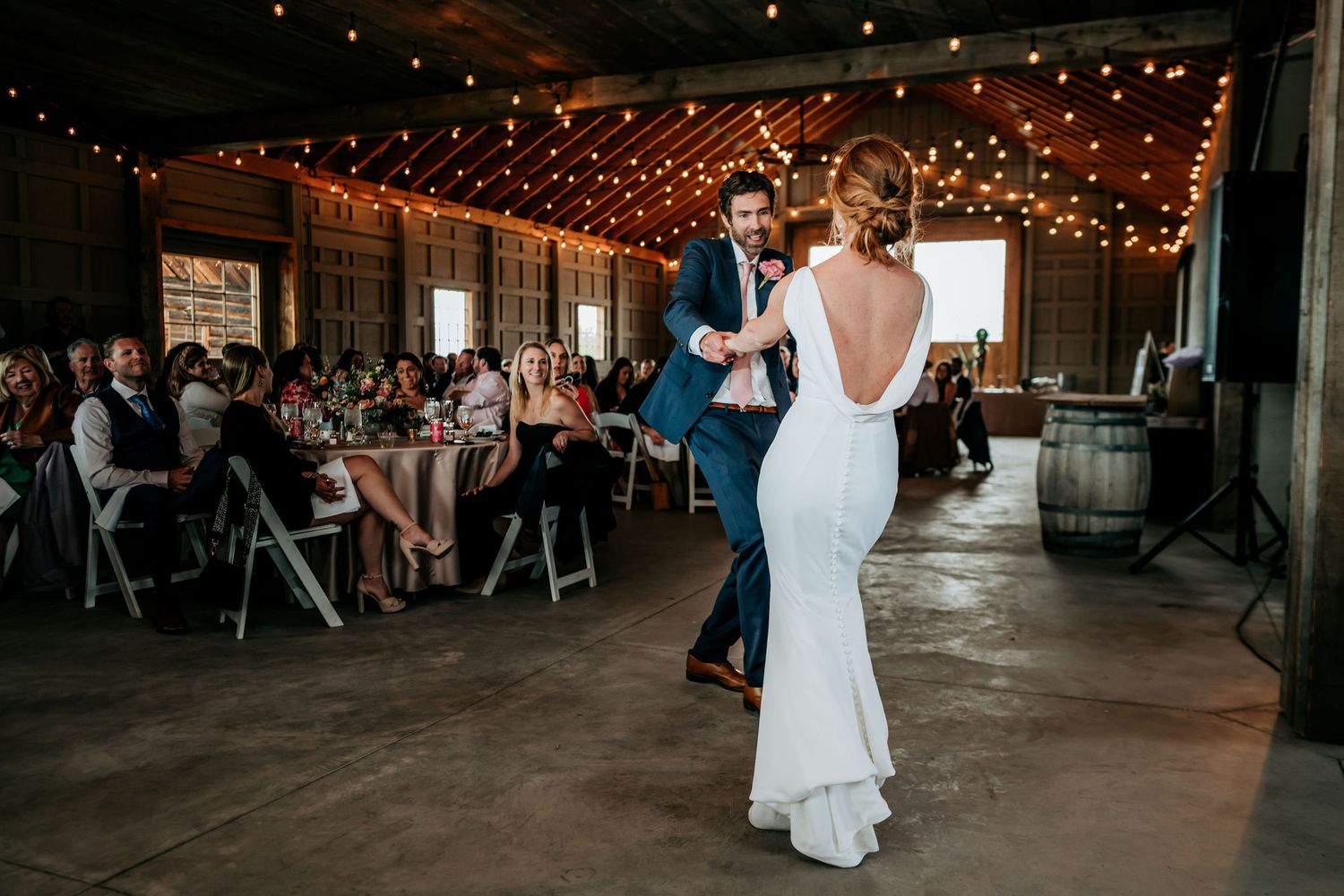 Newlyweds share their first dance in an industrial-style venue with guests watching from tables.