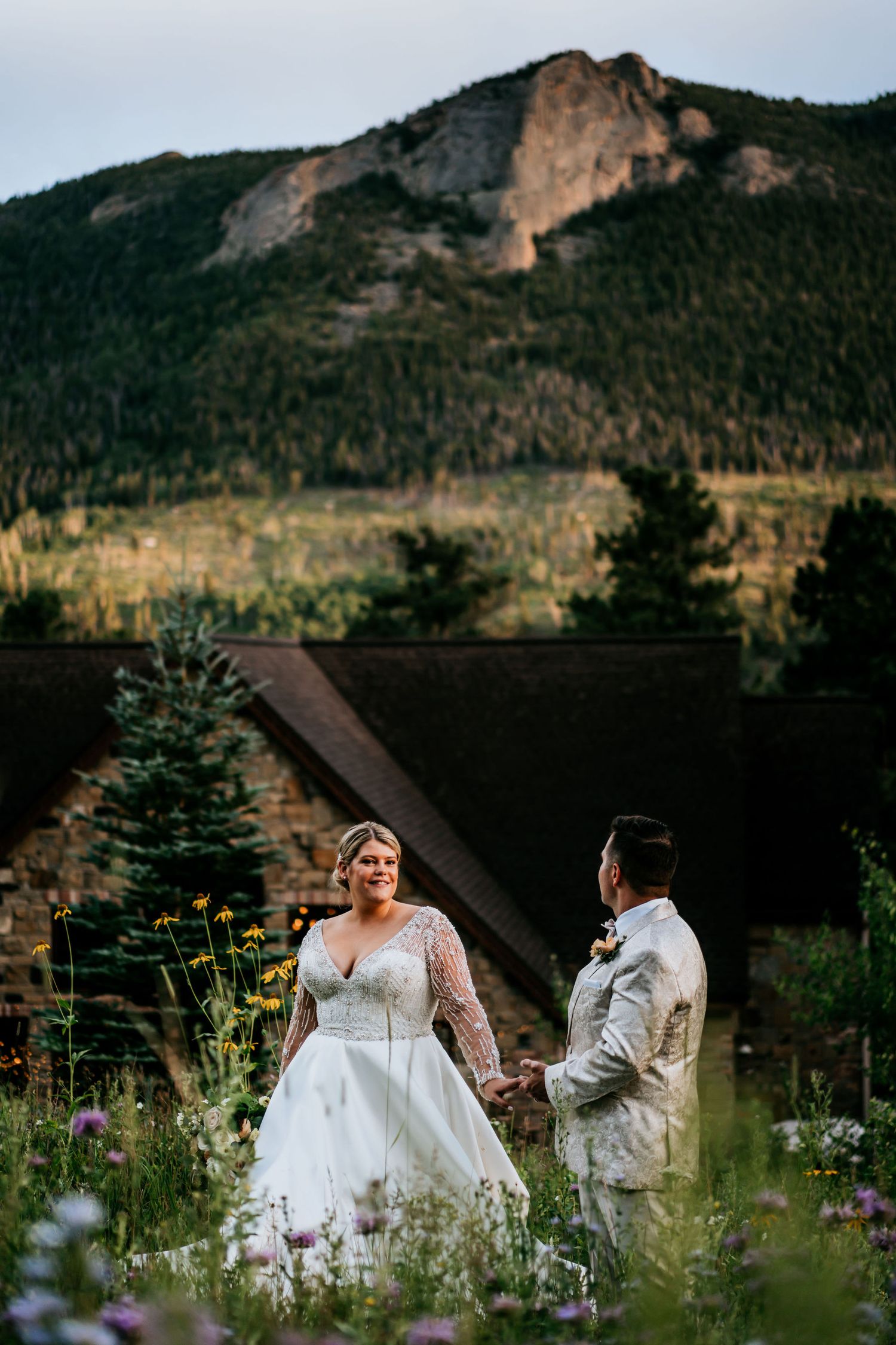 Mountain backdrop frames couple in garden with wildflowers during sunset wedding portraits.