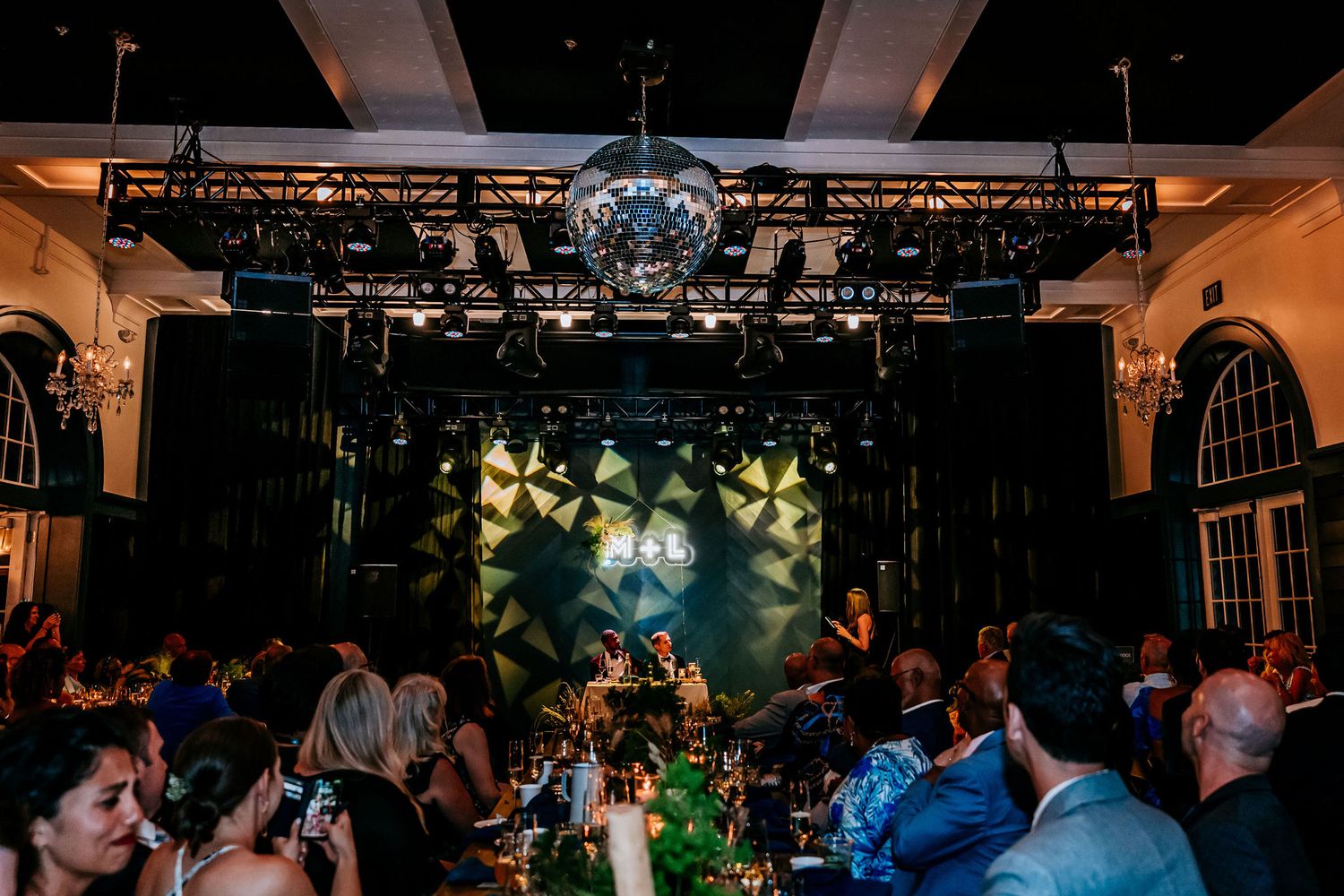 Wedding venue with dramatic stage lighting and geometric patterns above dancing guests.