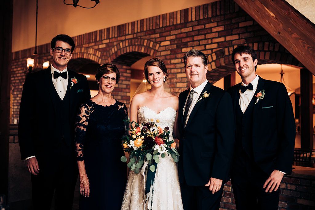 Formal wedding party group photo in front of brick wall with modern decor.