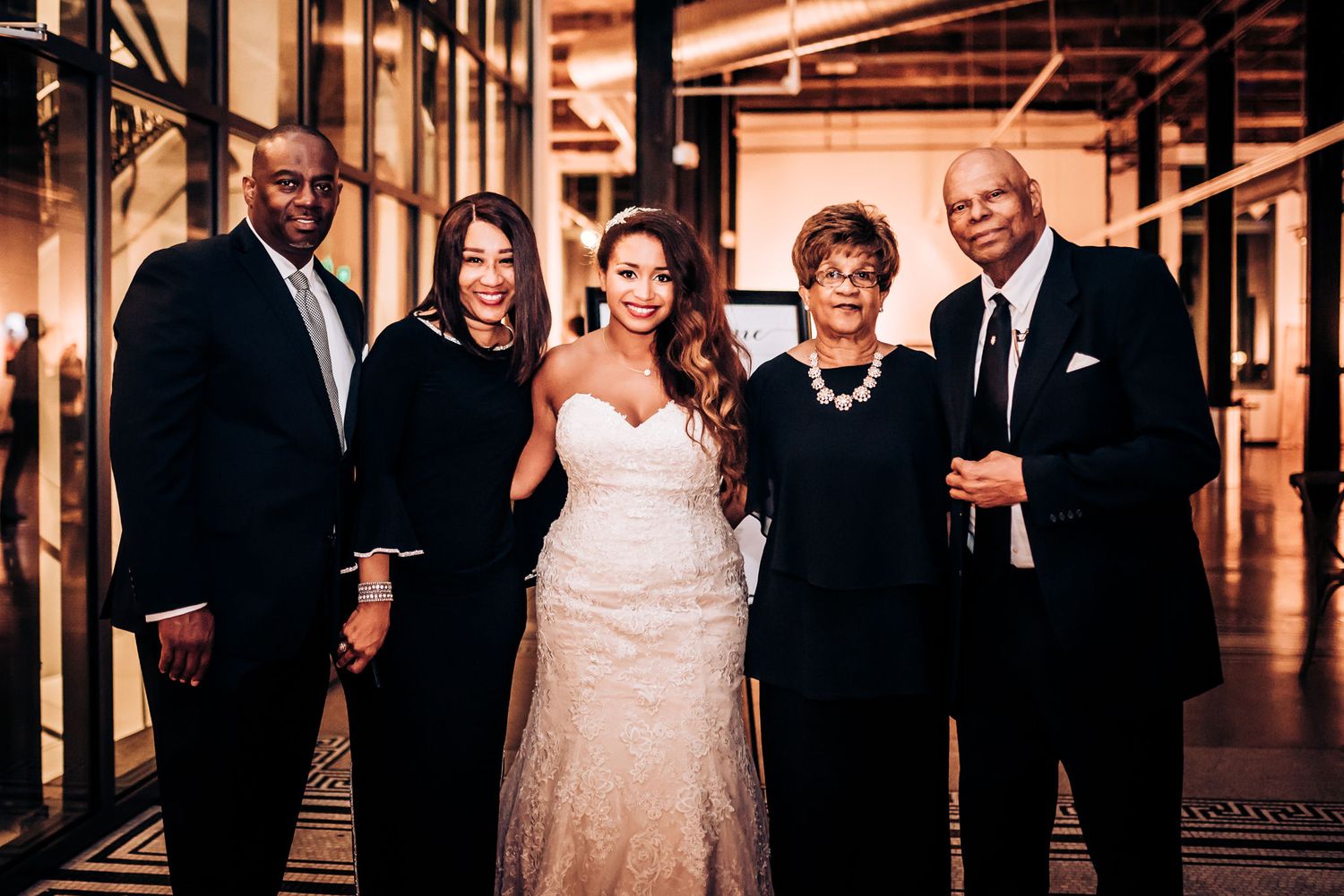 Wedding party members pose together in formal attire in an elegant venue hallway.