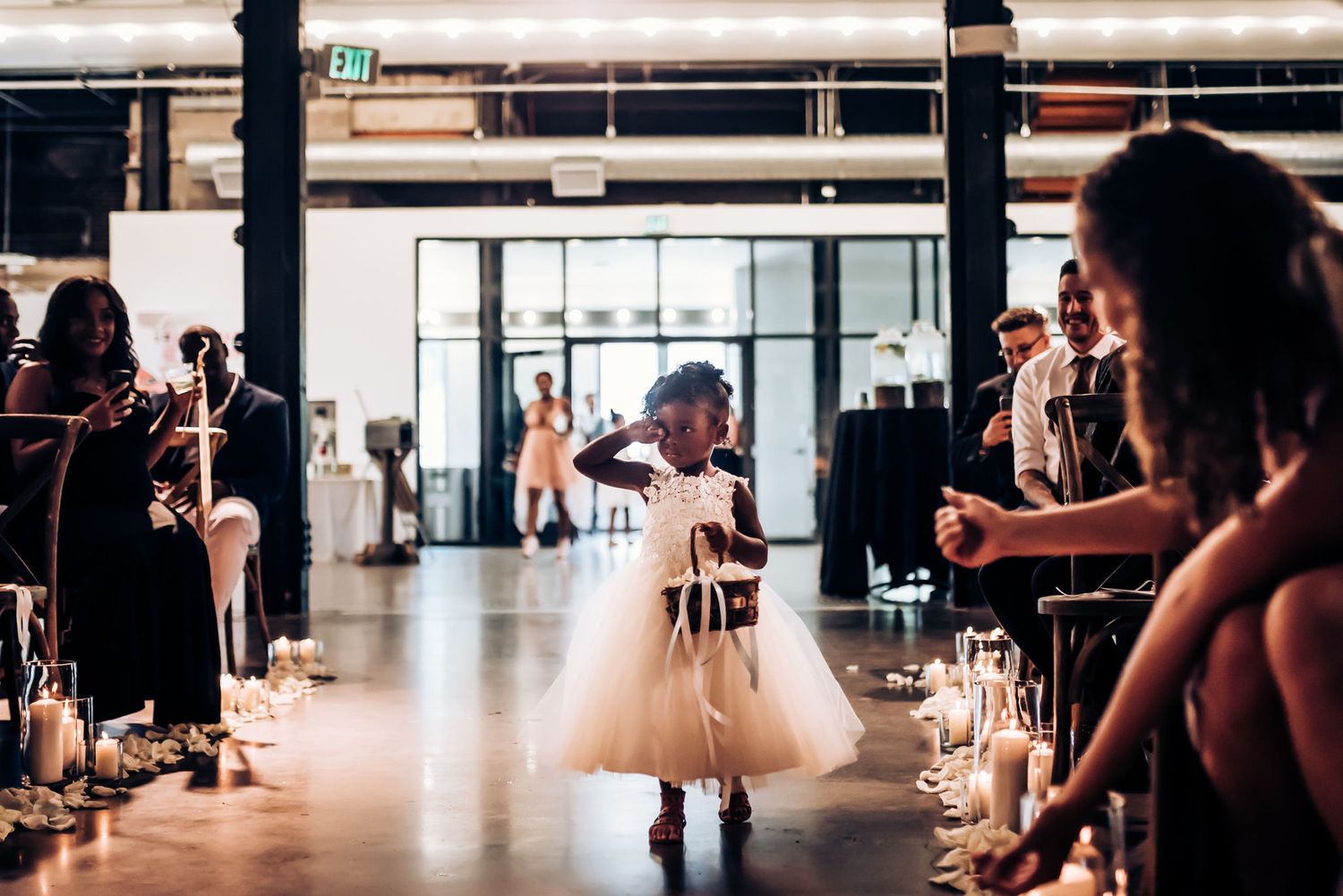 A child in a flowing white dress dances on a polished floor during a wedding reception.