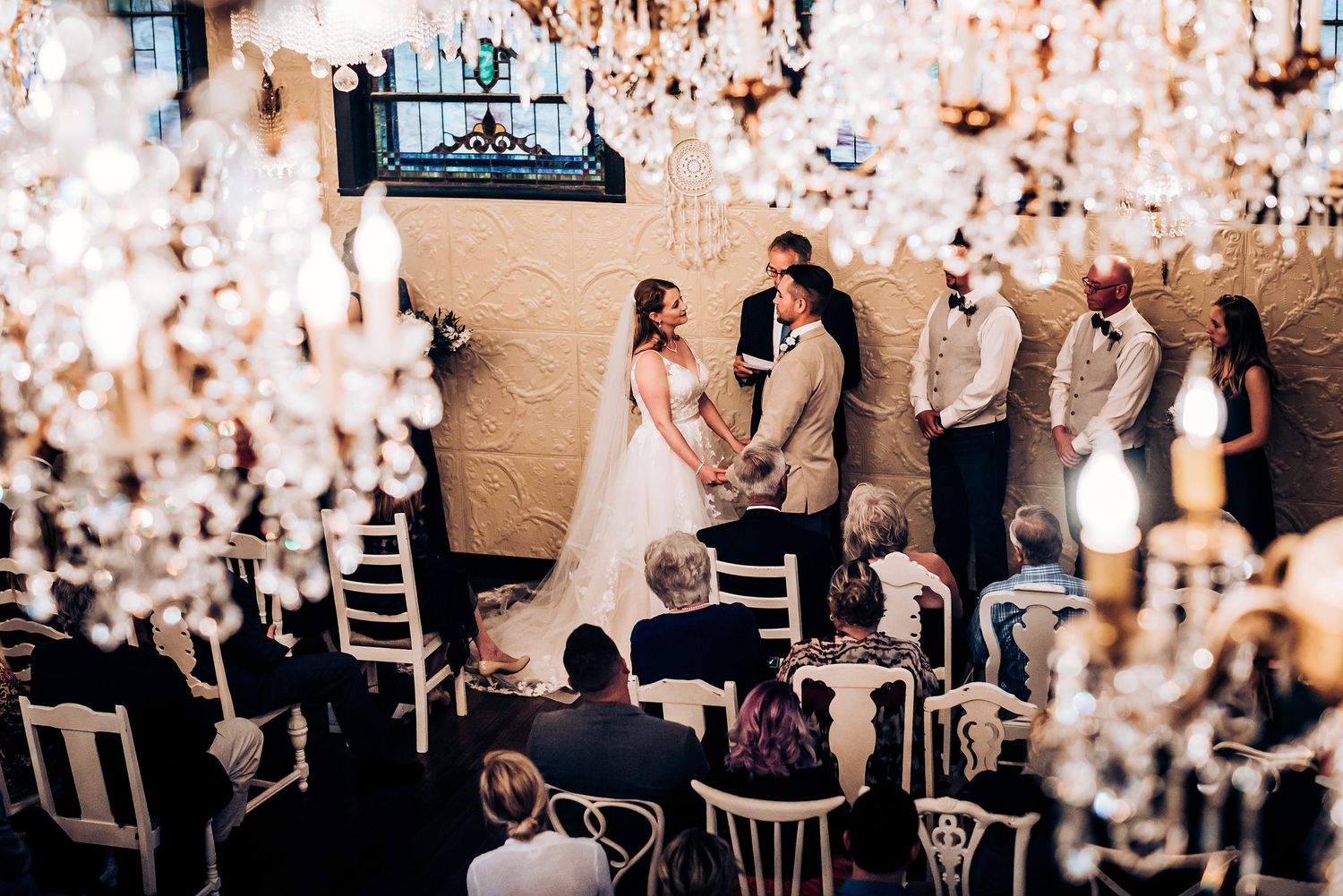 Wedding ceremony surrounded by sparkling crystal chandeliers in an intimate venue setting.