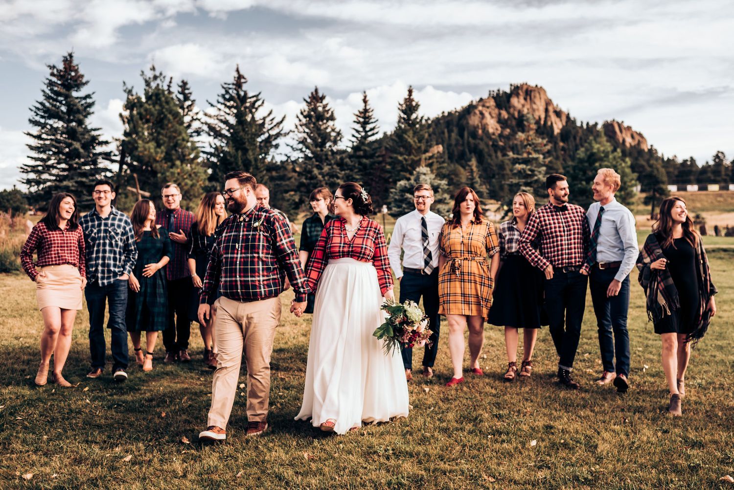 Wedding party poses for group photo with mountain backdrop and evergreen trees.