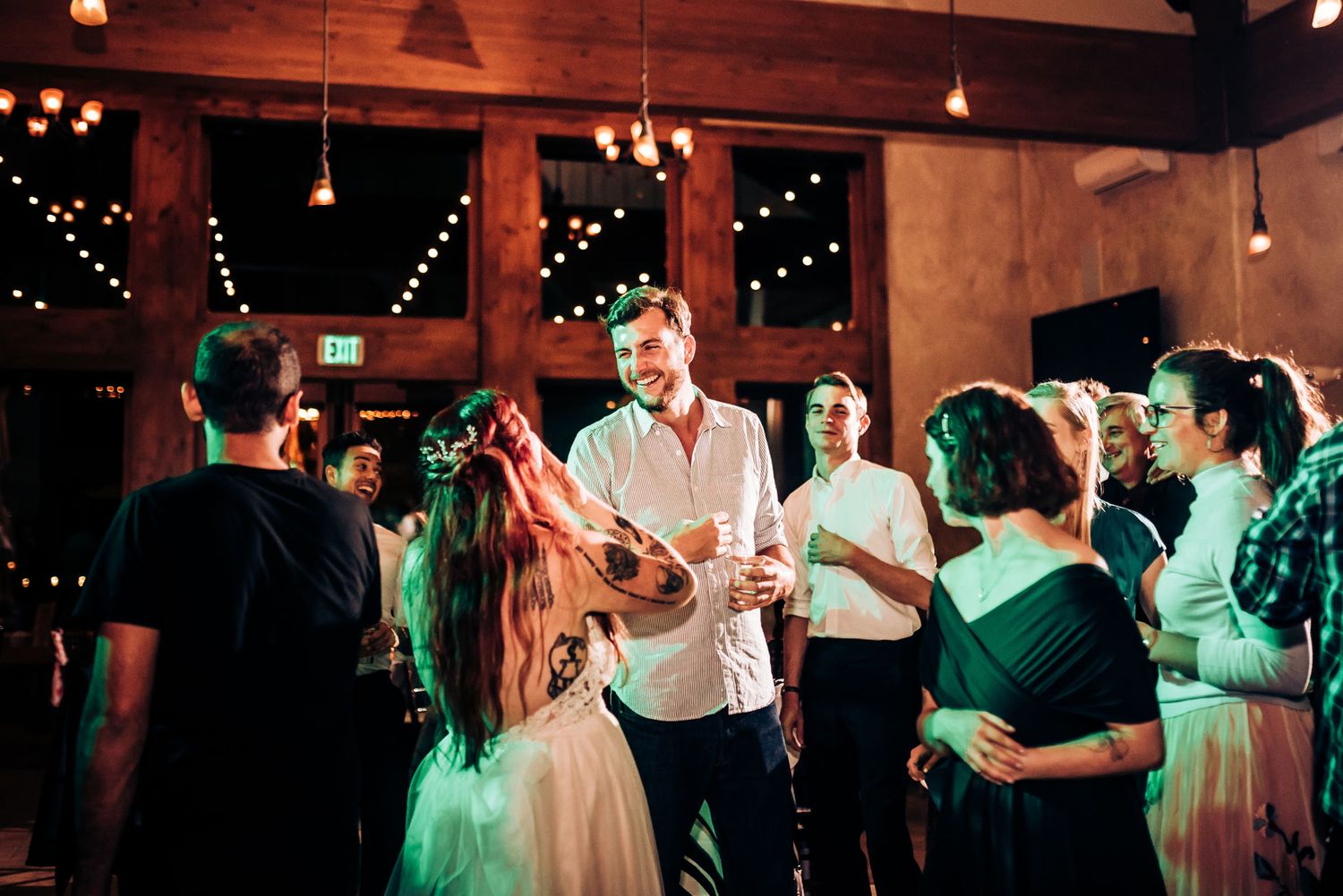 Guests mingle and celebrate at a wedding reception under twinkling lights in a rustic indoor venue.