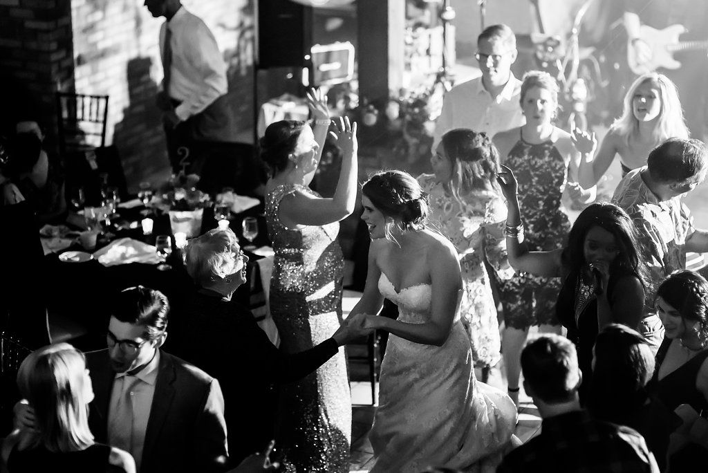 Black and white candid shot of wedding reception dance floor filled with celebrating guests.