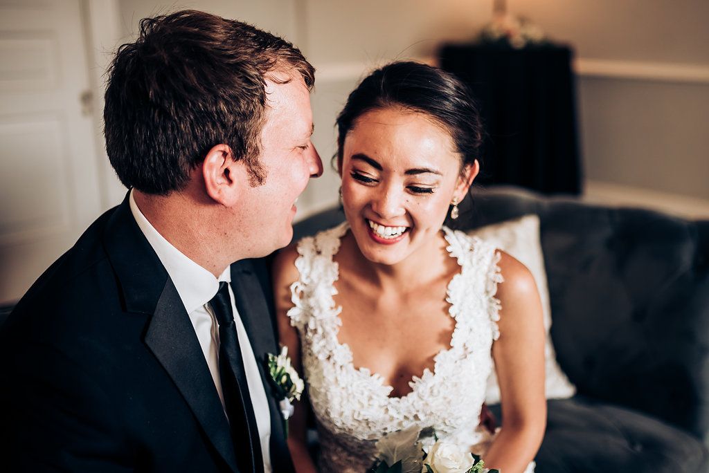 Wedding couple shares an intimate moment while sitting on a dark couch in their formal attire.