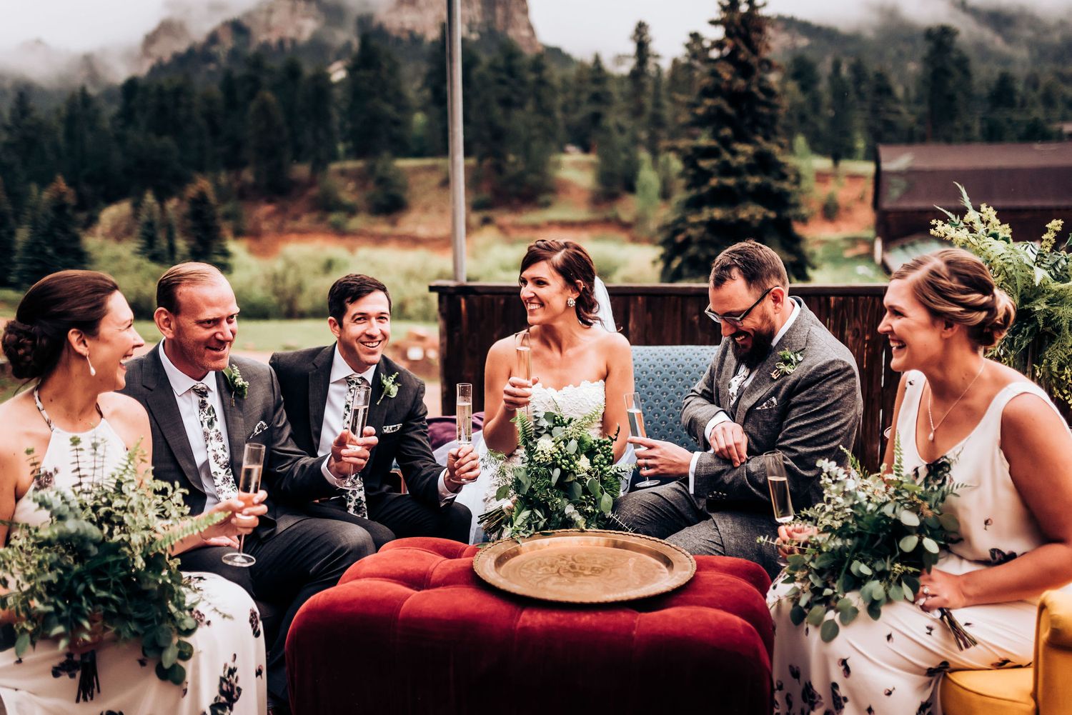 Wedding party shares drinks and laughs during outdoor mountain celebration.