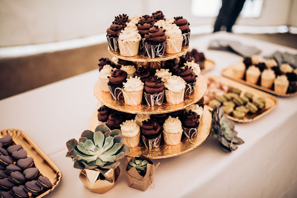 Three-tiered dessert stand with chocolate cupcakes and succulent decorations at a wedding reception.