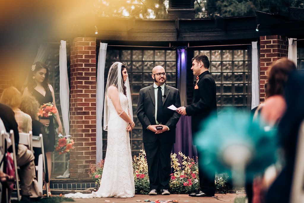 Outdoor wedding ceremony with brick architectural details and gathered guests.