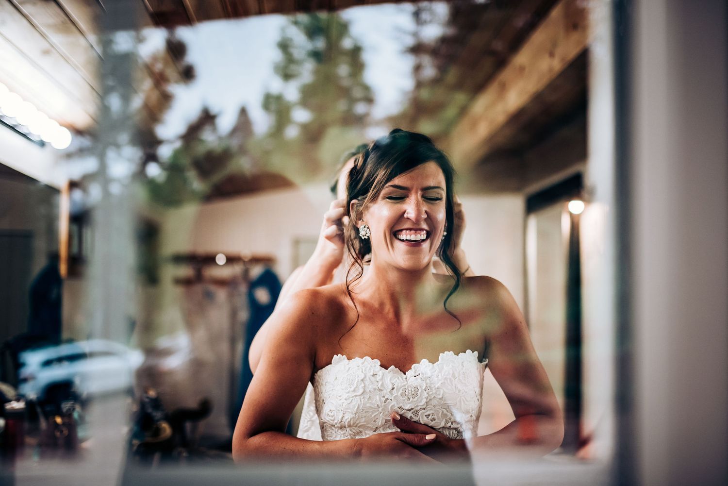 Joyful woman in a white lace wedding dress laughs during preparation.