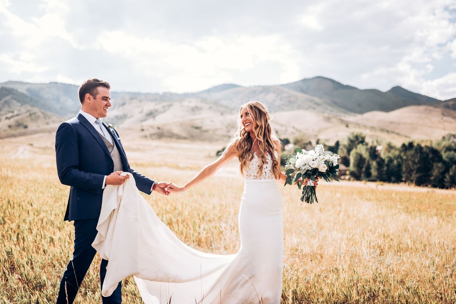 Beautiful wedding moment captured in mountain field with flowing dress and natural scenery.