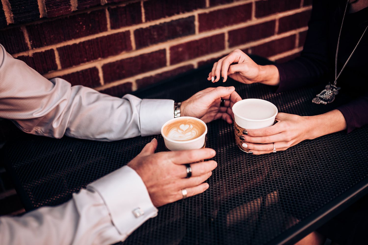 Close-up of hands holding coffee cups during romantic cafe date.
