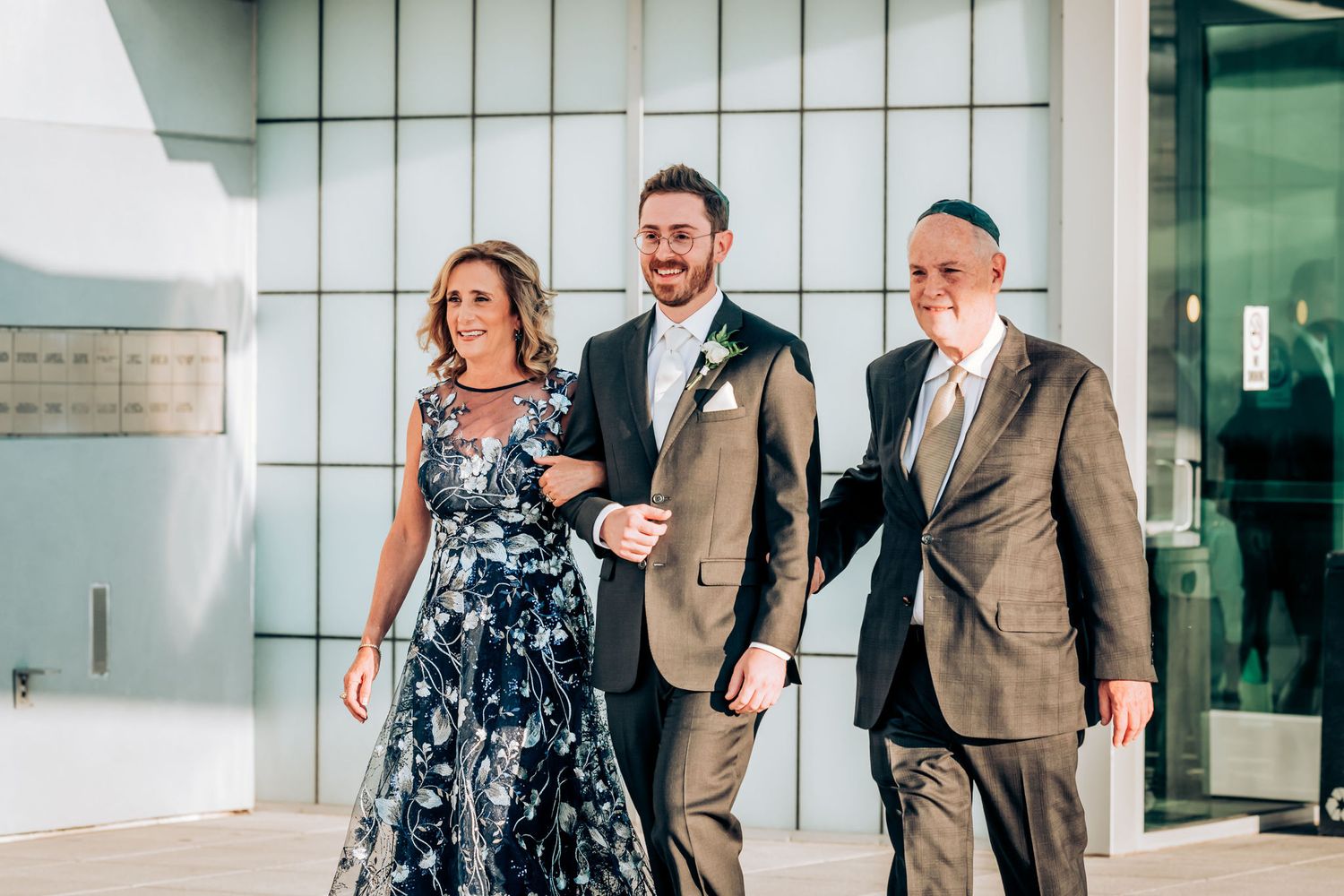 Wedding party members walk down modern architectural corridor during processional.